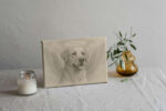 A memorial canvas print of a dog with wings and a halo on a white sheet next to a lit candle
